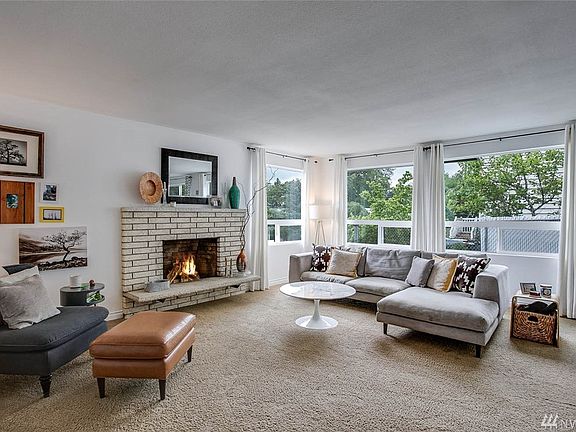 The living room is bathed in light from the three large picture windows