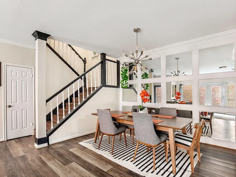 Dining area with a full-size table, statement light fixture, and mirrored wall that opens the space near the staircase.