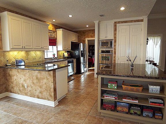 Kitchen offering tile flooring, granite counter tops, tumbled marble back splash, built-in stainless microwave and double oven, flat surface cook top, granite island workspace, pantry, crown molding and recessed lighting.