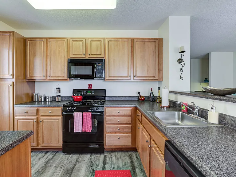 Kitchen with hardwood-style flooring, honey upper and lower cabinets with ample countertop space and black oven with mounted microwave above at Summit Place apartments in Methuen, MA.