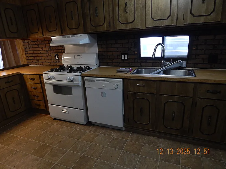 kitchen area showing cooking range with vent hood -dish washer -kitchen sink (has curtain rods in sink, which will be at the window).