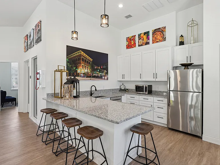 Contemporary kitchen with sleek granite countertops, elegant white cabinetry, and stainless steel appliances, complemented by stylish wooden bar stools and vibrant wall art.
