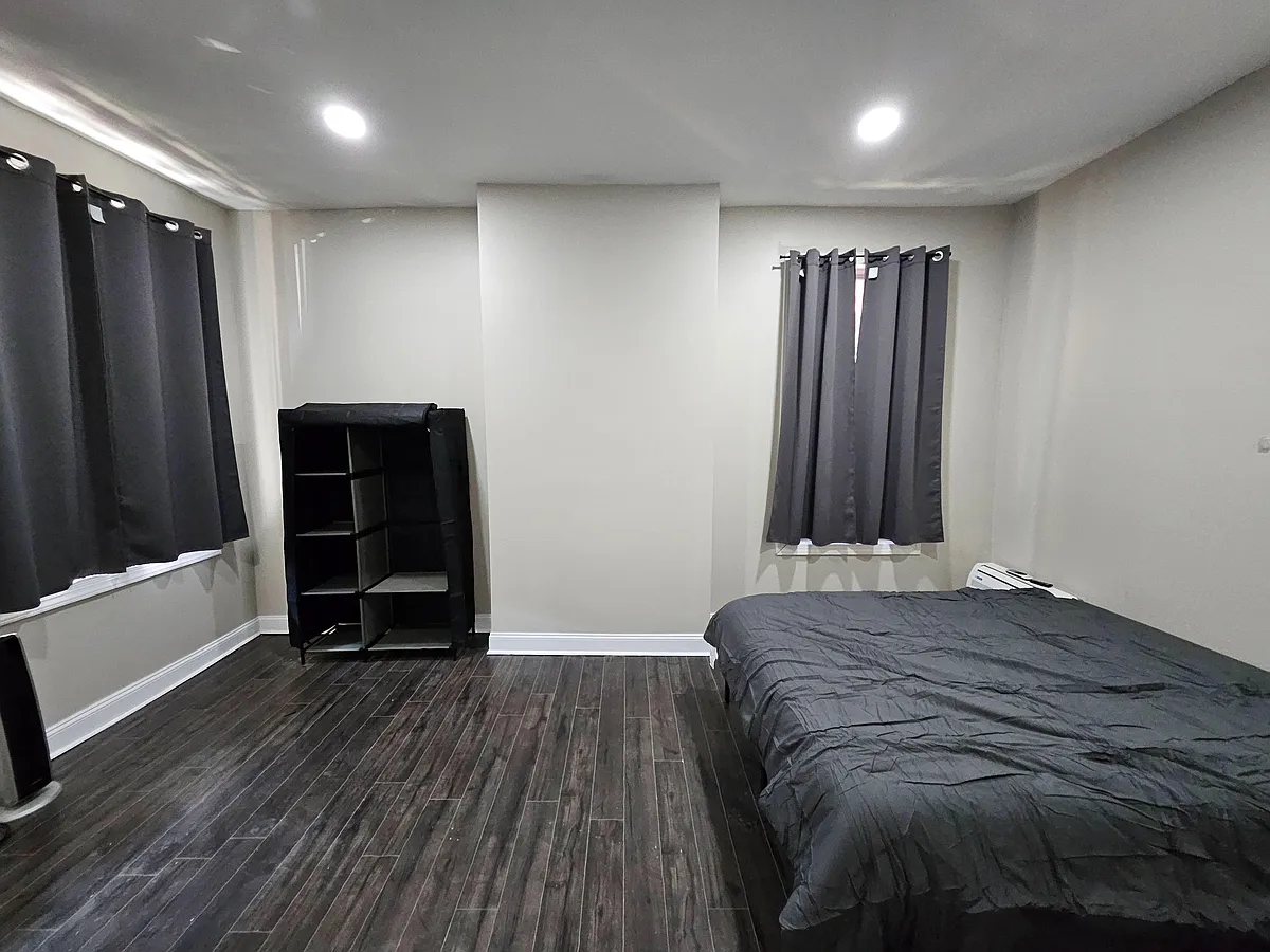 Spacious bedroom featuring durable wood-look flooring, recessed lighting, two windows with curtains, and open shelving. - N Broom St