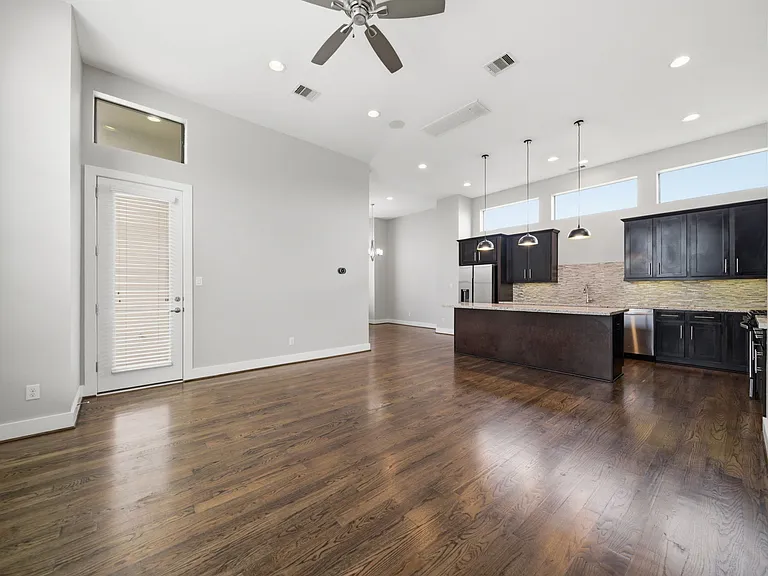 Expansive open-concept living space featuring rich hardwood floors, soaring ceilings, and abundant natural light. The modern kitchen is beautifully appointed with sleek dark cabinetry, a large island, and elegant pendant lighting.