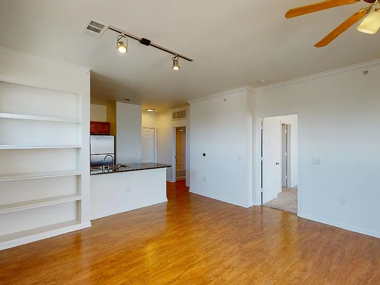 Apartment kitchen with stainless steel appliances, dining and living room with wood-style flooring.
