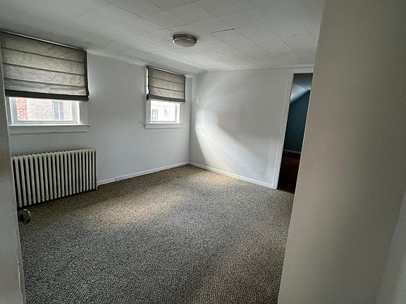 The living room is carpeted and freshly painted white. Has two windows.