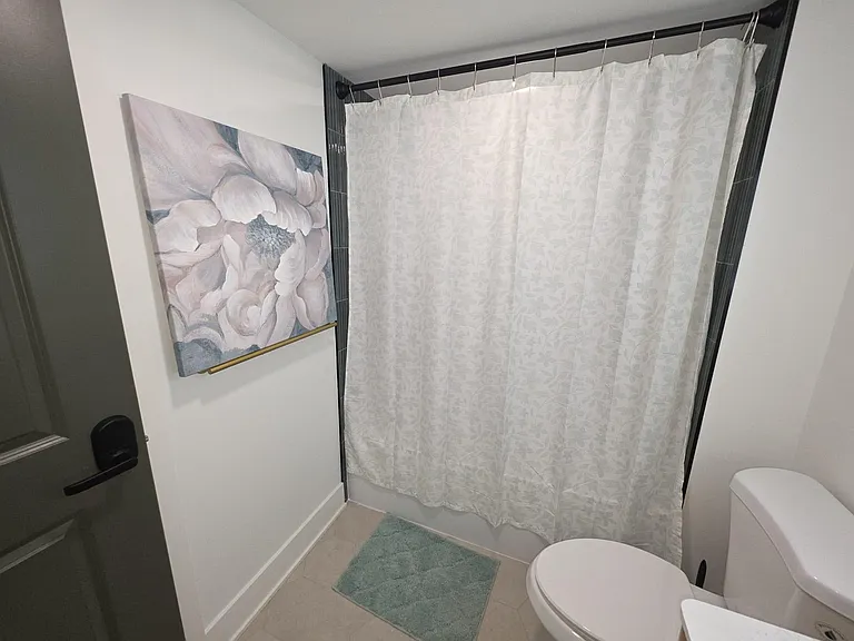 Full bathroom with a shower/tub combo, tiled surround, and modern fixtures, complemented by clean finishes and wall art.