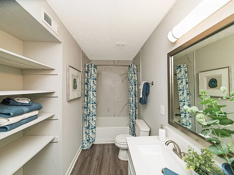 Bright bathroom with granite counters, built in shelving, and bathtub