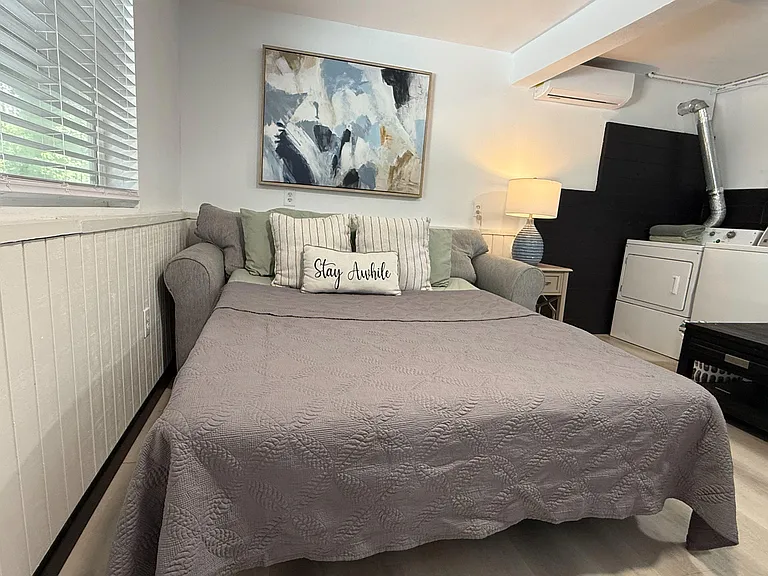 Furnished bedroom with a daybed, side table and lamp, plus a window for natural light and in-room laundry access.