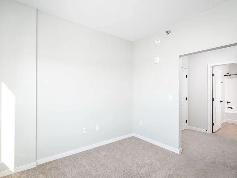 Bright, airy bedroom with neutral walls and carpet, leading to a modern en-suite bathroom featuring sleek finishes. Bright, airy bedroom with neutral walls and carpet, leading to a modern en-suite bathroom featuring sleek finishes.