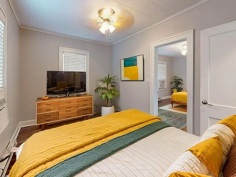 Charming bedroom with vibrant decor, featuring a cozy bed, chic wooden dresser, and modern artwork, bathed in natural light.