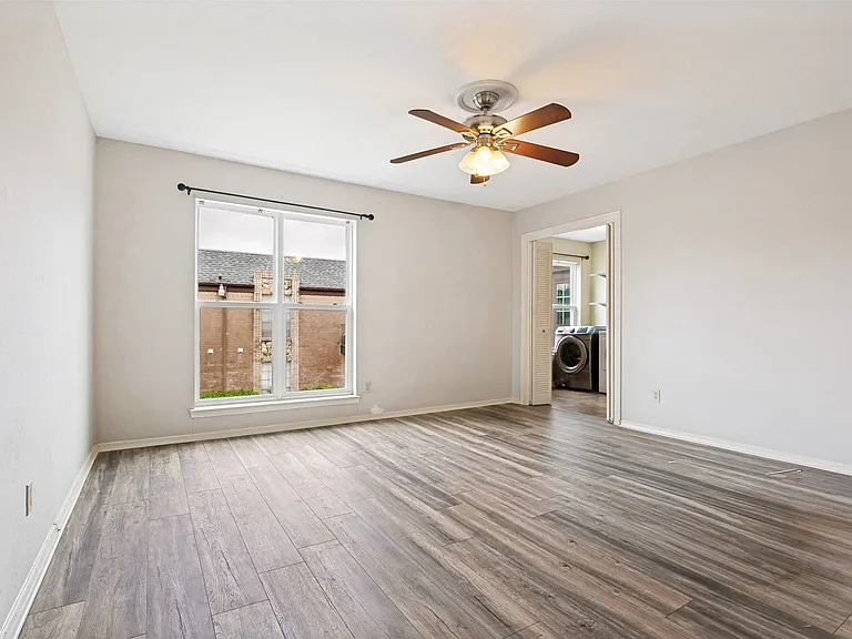 Light-filled room featuring wood-finish flooring, a ceiling fan with integrated lighting, and a white-trimmed window