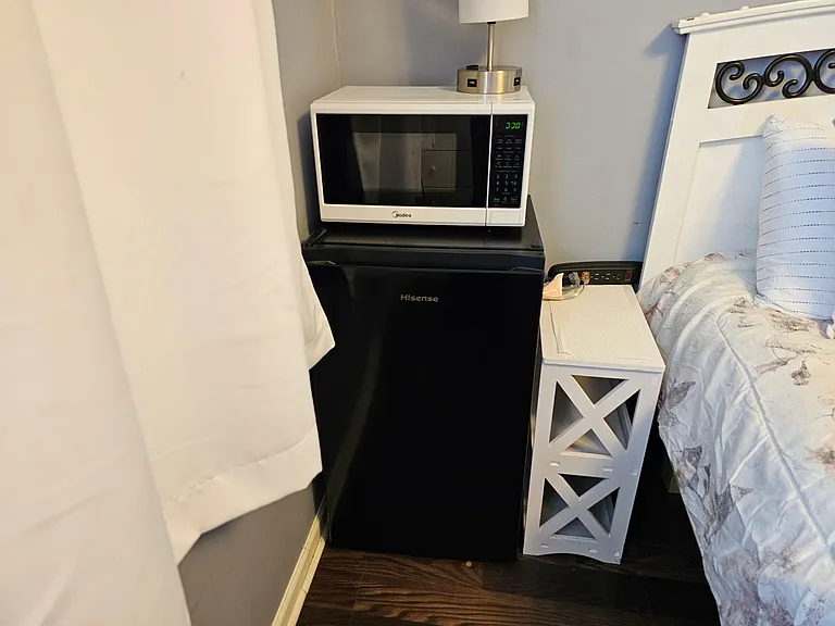 Bedroom includes convenient in-room amenities with a compact mini-fridge, microwave, and bedside table for daily comfort.