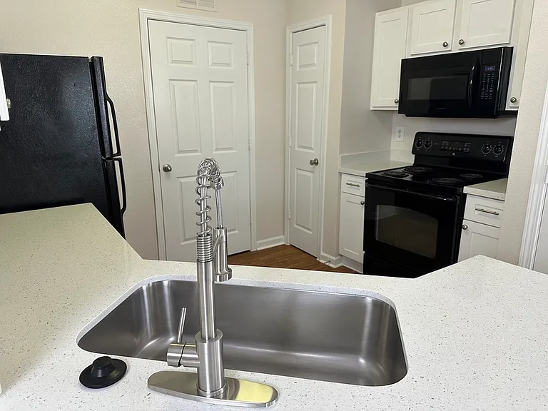 Modern kitchen with sleek black appliances, quartz countertops, elegant white cabinetry, and a chic stainless steel sink. Modern kitchen with sleek black appliances, quartz countertops, elegant white cabinetry, and a chic stainless steel sink.