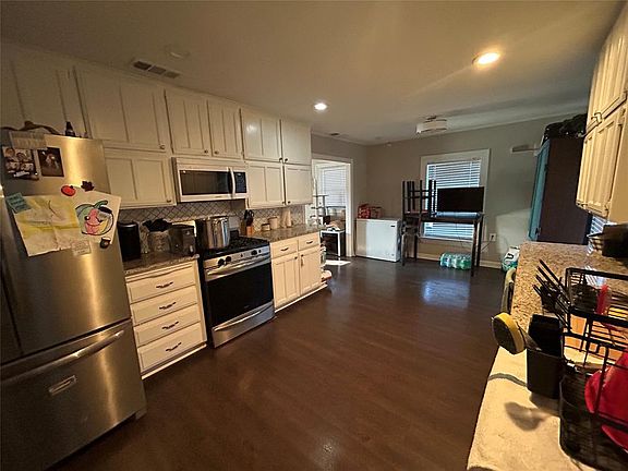 Kitchen with appliances with stainless steel finishes, tasteful backsplash, dark wood-style floors, dark stone countertops, and recessed lighting