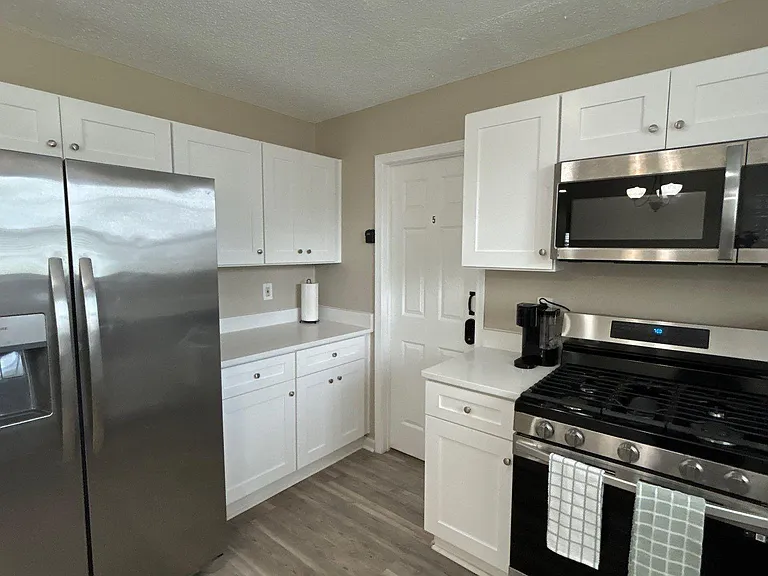 Updated kitchen with white cabinetry, ample counter space, and stainless steel refrigerator, range, and microwave.