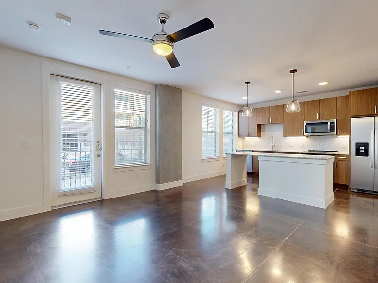 Apartment kitchen with stainless steel appliances, dining and living room with polished concrete flooring.