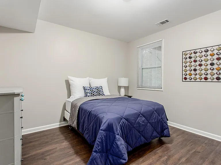 Bedroom with dresser, hanging rack, nightstand and lamp.
