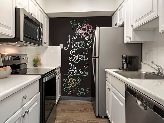 Renovated Package I kitchen with white cabinetry, laminate countertops, new stainless steel appliances, chalkboard accent wall, and hard surface flooring