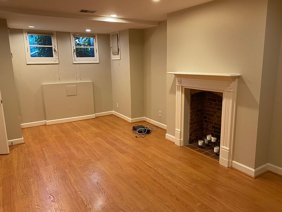 Spacious living room with wood floors, decorative fireplace, four windows.