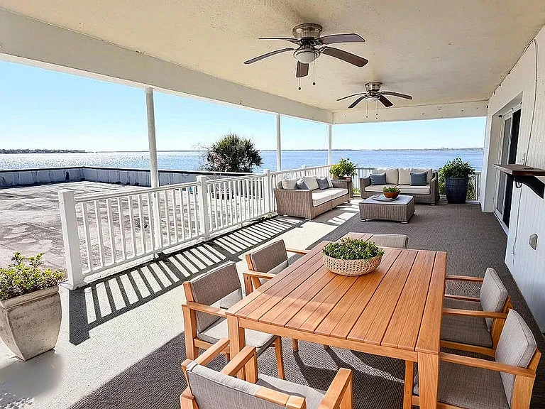 Spacious waterfront patio with elegant outdoor furniture, offering stunning views and relaxation under ceiling fans.