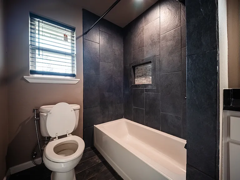 Full bathroom with tiled walls, bathtub, and natural light from window