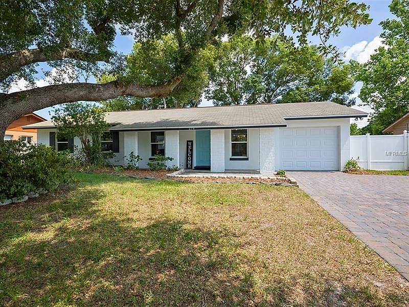 Lovely front yard with pavered driveway, mature landscaping, and shade trees.