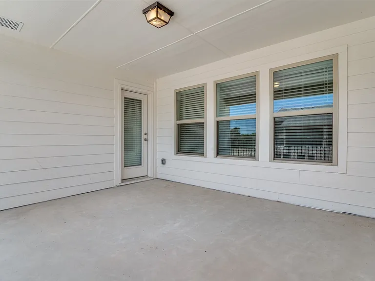 Covered outdoor patio space with a concrete slab, white plank siding, a frosted glass panel door, and multiple windows with blinds