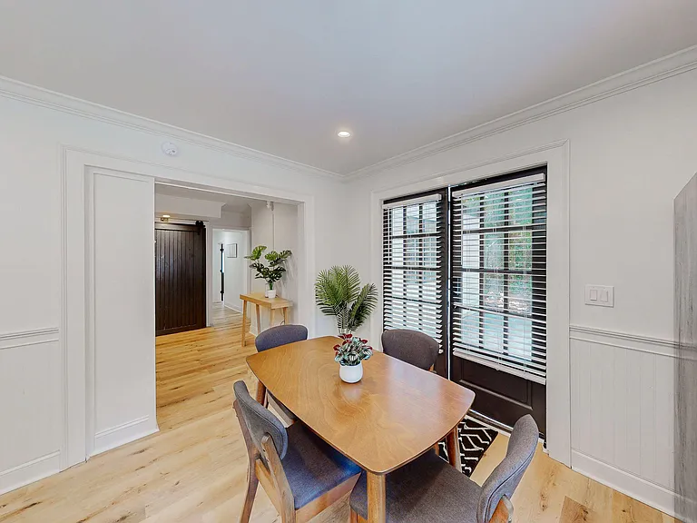 Dedicated dining area with a table for four, hardwood-style floors, and large windows with blinds for natural light.