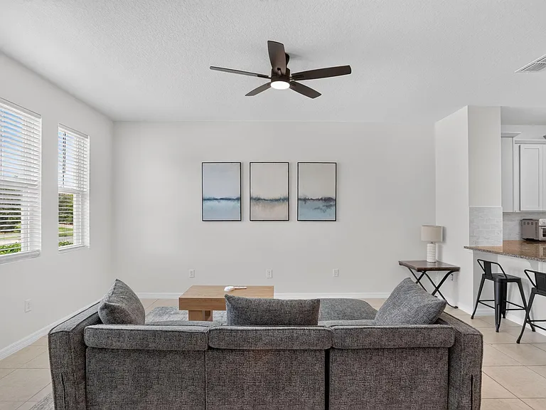 Open living area with a ceiling fan, large windows with blinds, and easy flow to the breakfast bar and kitchen.