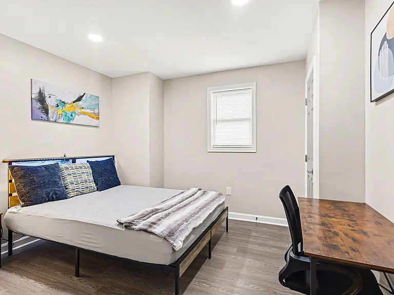 Furnished bedroom with a full bed, desk setup, and a window with blinds in a neutral, easy-to-decorate layout.
