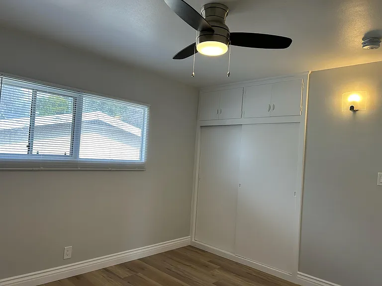 Inside bedroom and view of window, closets, blinds and brand new laminate floors with ceiling lamp/fan.