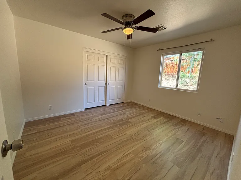 Bright bedroom with ceiling fan, closet, durable flooring, and natural light.