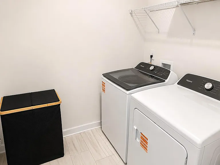Dedicated laundry room with full-size washer and dryer, overhead wire shelving, and space for hampers and supplies.