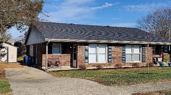 Left side of duplex, small front porch, side entrance with storage building.