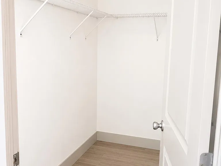 Spacious walk-in closet with wraparound wire shelving and durable flooring for easy organization and storage.