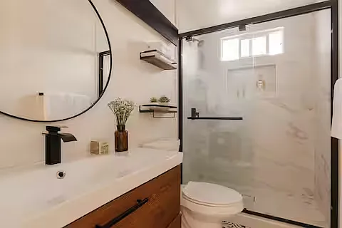 Bathroom 3
Stylish bathroom featuring a modern vanity with wood finish, round mirror, and walk-in shower with glass doors. Bright, clean design with black accents and natural light creates a fresh, contemporary feel.