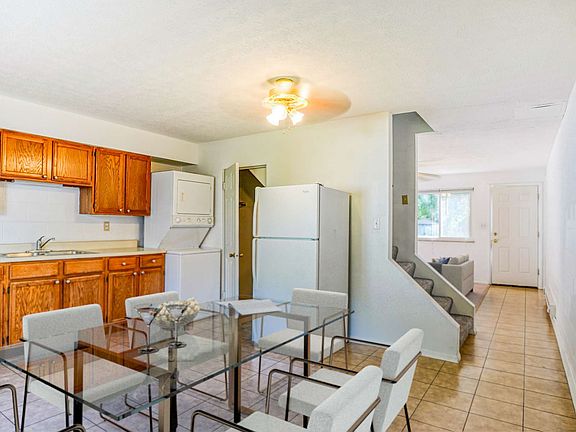 A kitchen with wooden cabinets, white appliances, a sink, and a ceiling fan, featuring tiled flooring.