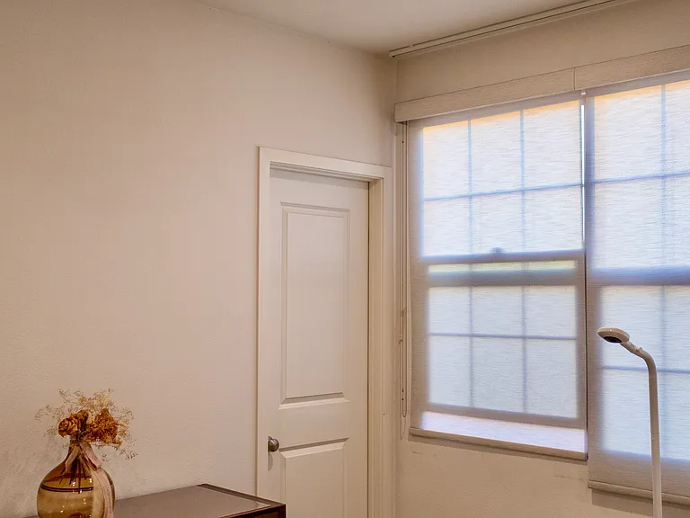 Primary Bedroom: Side view of the room showcasing the dresser layout next to the closed closet door, framed by the large window and overhead ceiling fan.