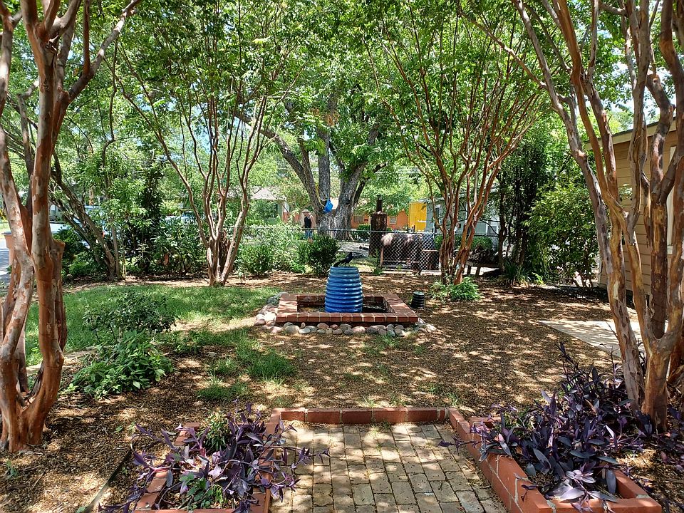 Side view of the front yard with ample shade provided by four Crepe Myrtle trees and a bench and chairs.