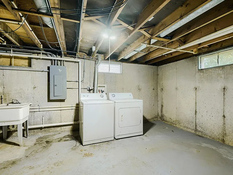 Basement laundry area with washer and dryer hookups, utility sink, and open floor space for storage and sorting.