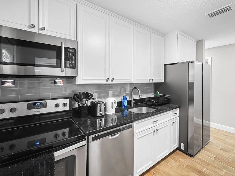 Kitchen with white cabinetry, subway-tile backsplash, stone-look counters, and stainless steel appliances for easy meal prep.