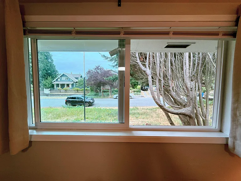 Large window with curtain panels offers a relaxing neighborhood view and brings in ample natural light.