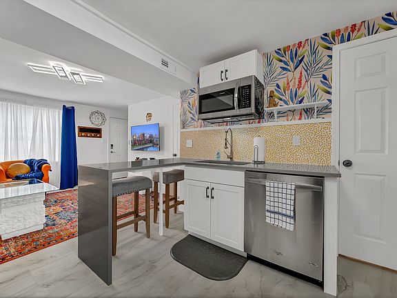 Kitchen island with a seating area, microwave, and dishwasher. To the right door to the utility room where the washer/dryer combo is located.