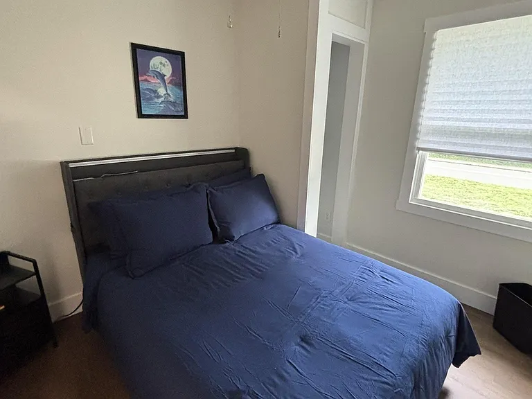 Furnished bedroom with a full bed, ceiling fan, and a window with blinds for natural light and privacy.