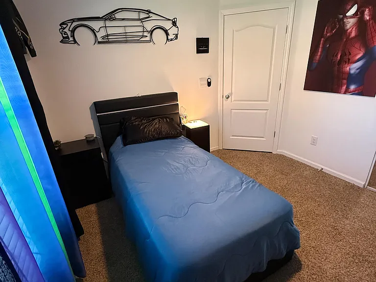 Carpeted bedroom with a twin bed, nightstand, and ceiling fan, offering a simple layout with room for personal storage.