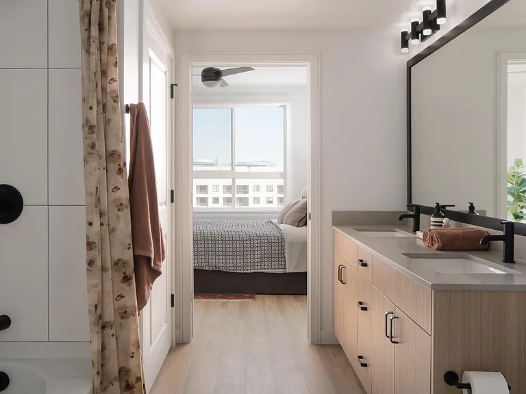 A bright bath with dual sinks, matte black fixtures, and a seamless flow into the bedroom beyond.