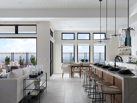 A modern, open-concept kitchen and living room with large windows overlooking a scenic outdoor view,