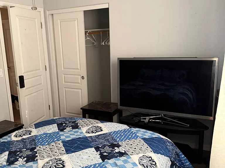 Furnished bedroom with a comfortable bed, TV setup, and a sliding-door closet for convenient storage.