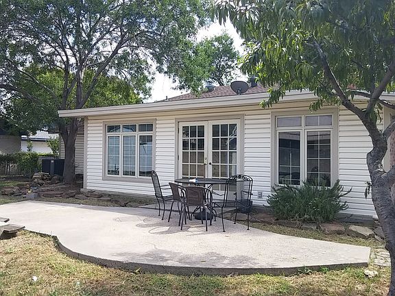 Sunroom, back patio with metal table and chairs. Large trees.
